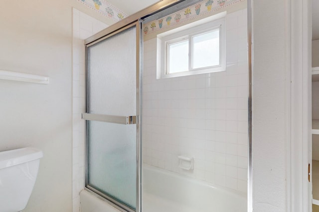 bathroom with bath / shower combo with glass door and toilet