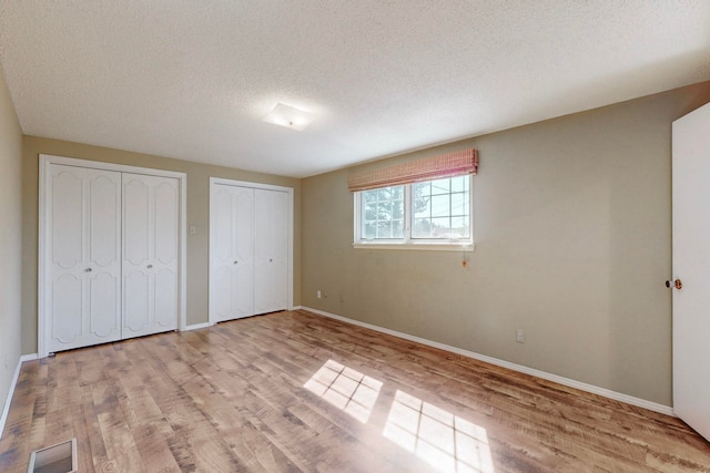 unfurnished bedroom featuring multiple closets, a textured ceiling, and light hardwood / wood-style flooring