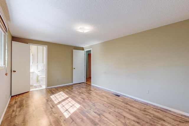 unfurnished bedroom featuring a textured ceiling, ensuite bath, and light hardwood / wood-style floors