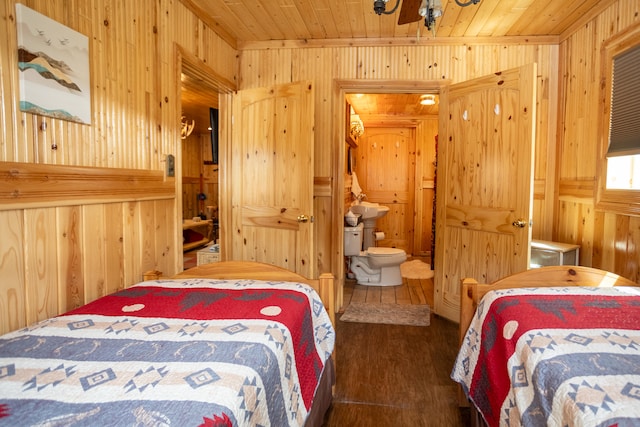 bedroom with connected bathroom, wood walls, wooden ceiling, and dark hardwood / wood-style flooring