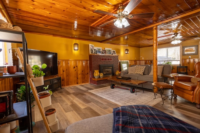 living room with ceiling fan, wooden ceiling, wood-type flooring, a brick fireplace, and wooden walls