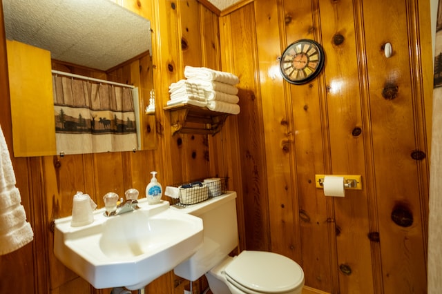 bathroom with sink, a shower with shower curtain, toilet, and wood walls