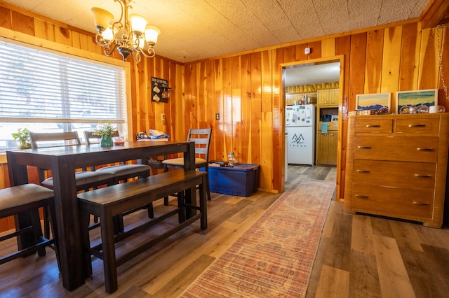 dining room with a notable chandelier, hardwood / wood-style floors, and wooden walls