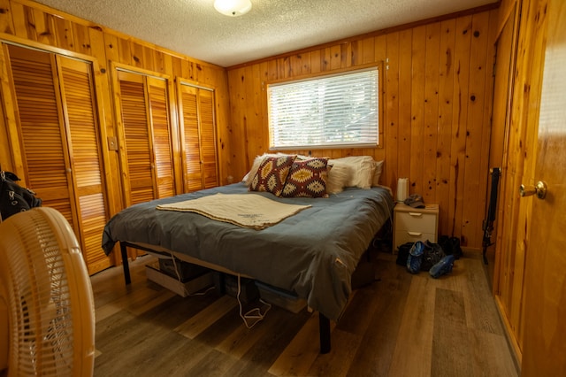 bedroom with multiple closets, a textured ceiling, wooden walls, and hardwood / wood-style floors