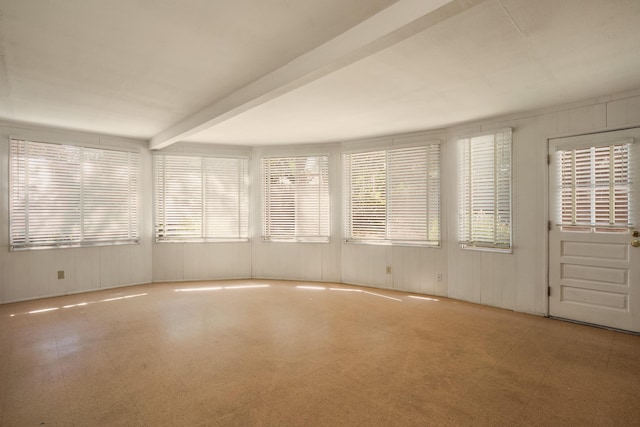 unfurnished room featuring beamed ceiling and a healthy amount of sunlight