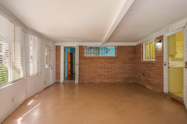 unfurnished room with brick wall and beam ceiling