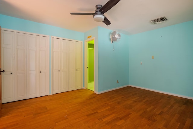 unfurnished bedroom featuring ceiling fan, hardwood / wood-style flooring, and multiple closets