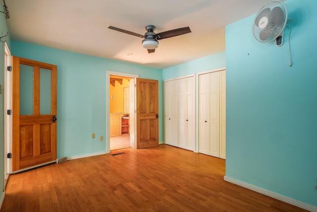 unfurnished bedroom with ceiling fan, wood-type flooring, and two closets