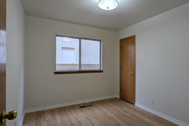 unfurnished room with a textured ceiling and light hardwood / wood-style floors