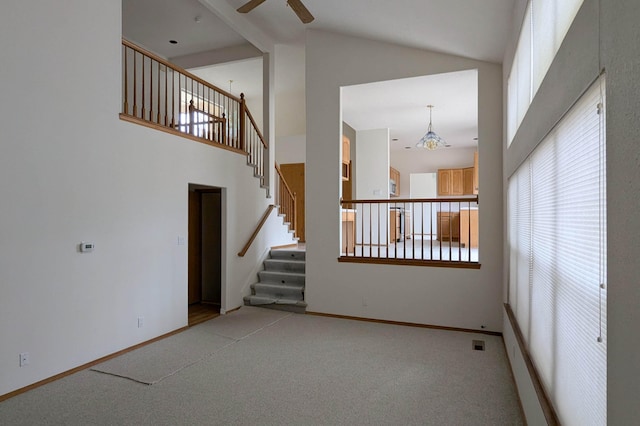 unfurnished living room featuring high vaulted ceiling, carpet floors, and ceiling fan with notable chandelier