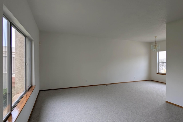 carpeted spare room with an inviting chandelier