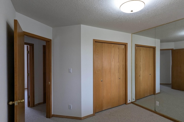 unfurnished bedroom featuring a textured ceiling, multiple closets, and light colored carpet