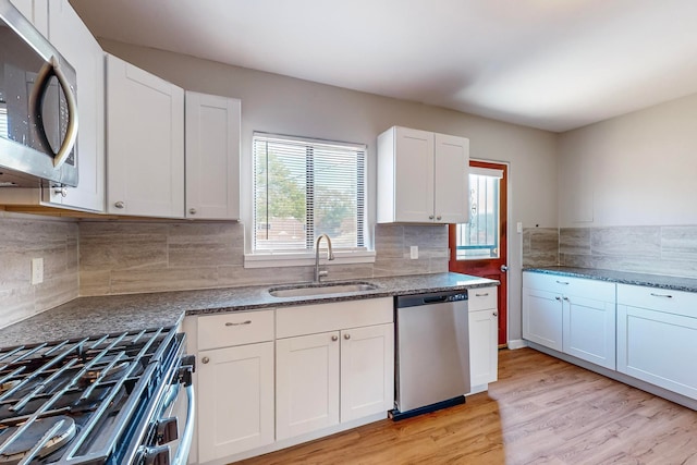 kitchen with appliances with stainless steel finishes, white cabinetry, sink, and light hardwood / wood-style floors