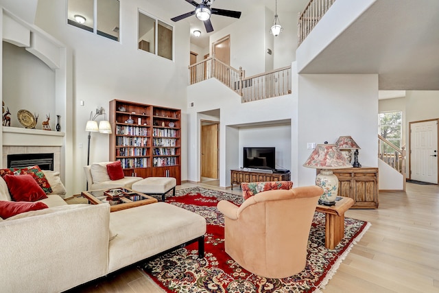 living room with a towering ceiling, a fireplace, light hardwood / wood-style floors, and ceiling fan