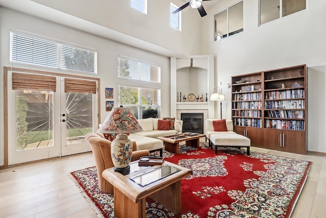 living room with a high ceiling, light hardwood / wood-style flooring, a fireplace, and ceiling fan