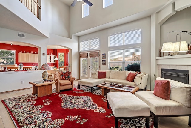 living room with a high ceiling, a tiled fireplace, hardwood / wood-style flooring, and ceiling fan