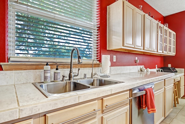 kitchen featuring light tile patterned floors, cream cabinets, sink, and stainless steel dishwasher