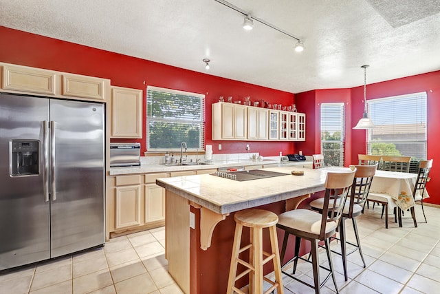 kitchen with decorative light fixtures, light tile patterned floors, a textured ceiling, stainless steel refrigerator with ice dispenser, and a center island