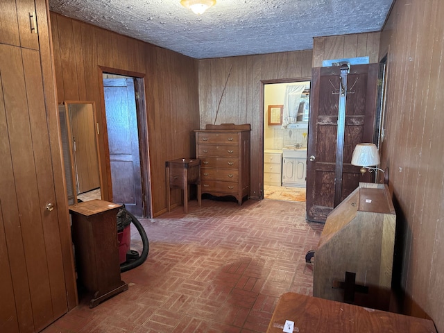 bedroom featuring wood walls, ensuite bath, and a textured ceiling