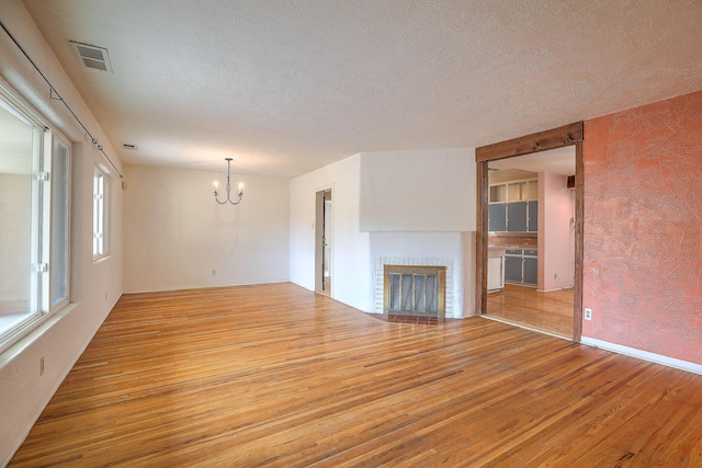 unfurnished living room featuring a textured ceiling, a brick fireplace, wood-type flooring, and an inviting chandelier