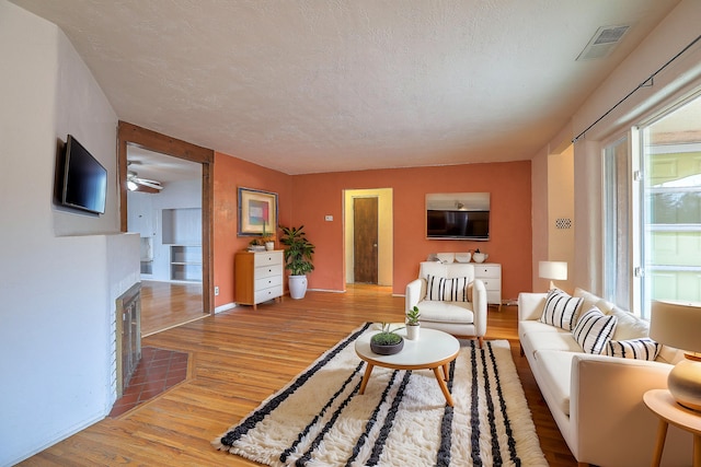 living room featuring light hardwood / wood-style floors, a textured ceiling, and ceiling fan