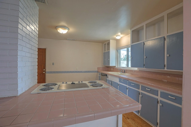 kitchen with tile countertops, sink, brick wall, and white electric cooktop