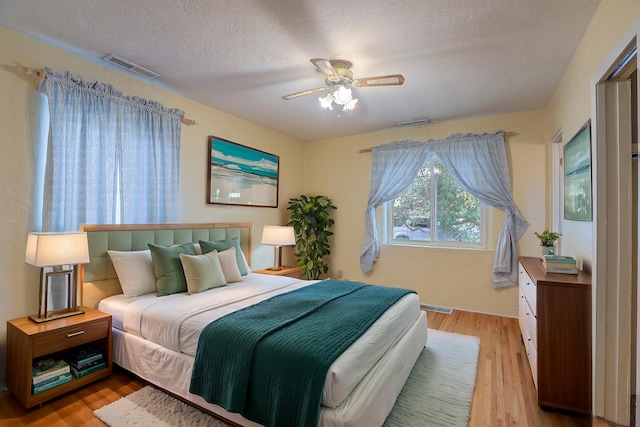 bedroom with a textured ceiling, light wood-type flooring, and ceiling fan