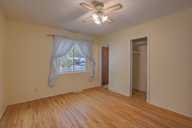 unfurnished bedroom featuring a spacious closet, light hardwood / wood-style flooring, a closet, and ceiling fan