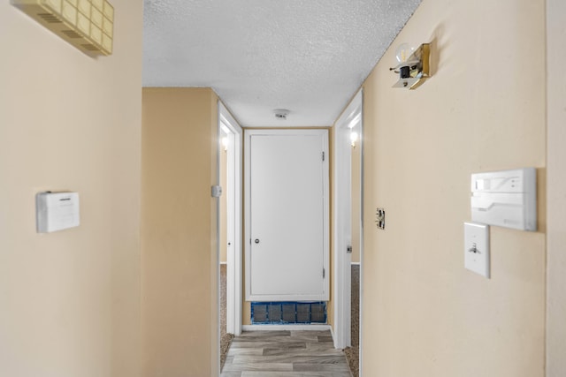 hall with a textured ceiling and light hardwood / wood-style flooring