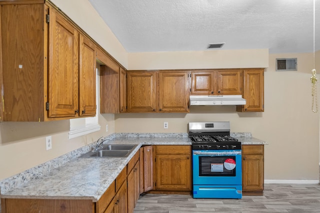 kitchen with gas range, a textured ceiling, sink, and light hardwood / wood-style floors