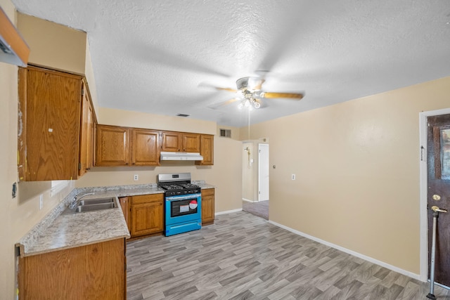 kitchen featuring gas stove, ceiling fan, a textured ceiling, light hardwood / wood-style flooring, and sink