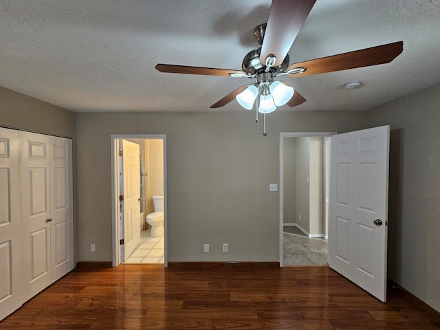 unfurnished bedroom featuring hardwood / wood-style flooring, a closet, ensuite bath, a textured ceiling, and ceiling fan