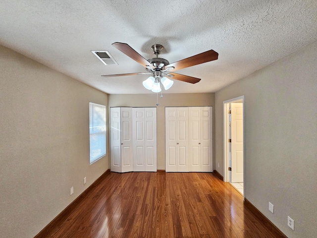 unfurnished bedroom with ceiling fan, wood-type flooring, a textured ceiling, and two closets