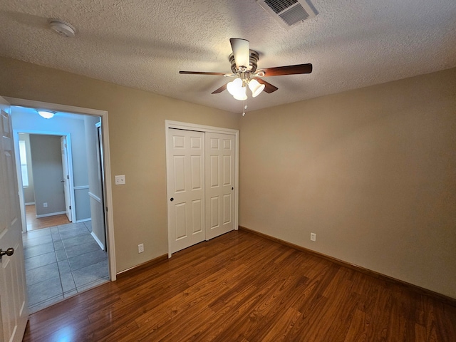 unfurnished bedroom featuring a closet, a textured ceiling, wood-type flooring, and ceiling fan