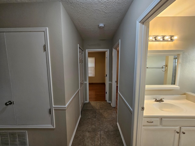 hall with a textured ceiling, sink, and dark tile patterned floors