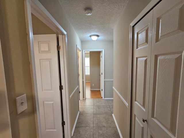 hallway with a textured ceiling and light tile patterned floors