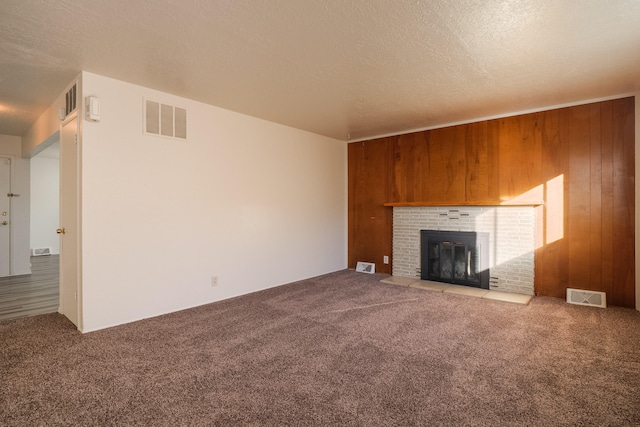 unfurnished living room featuring wood walls, a textured ceiling, a fireplace, and carpet floors