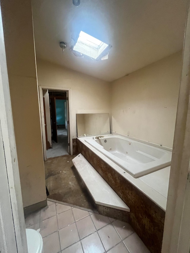 bathroom featuring toilet, a relaxing tiled tub, lofted ceiling with skylight, and tile patterned flooring