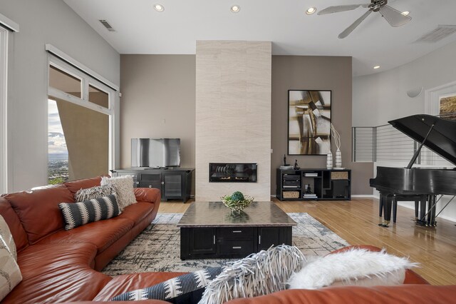 living room featuring a tiled fireplace, ceiling fan, and light hardwood / wood-style flooring