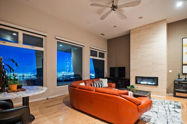 living room with ceiling fan, light wood-type flooring, and a tile fireplace