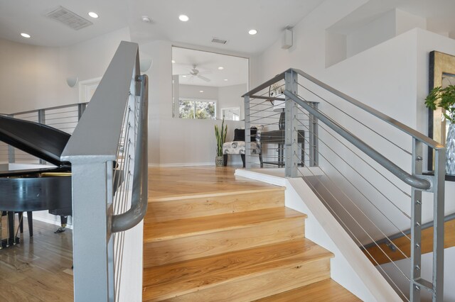 stairway with ceiling fan and wood-type flooring