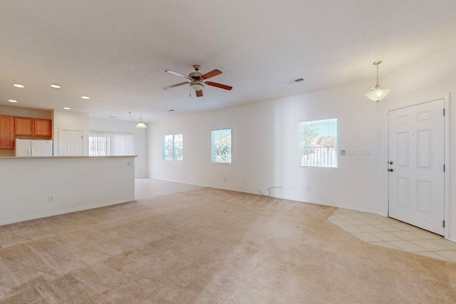 unfurnished living room featuring light carpet, ceiling fan, and a wealth of natural light