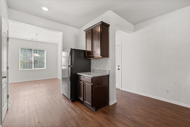 kitchen featuring light stone countertops, dark brown cabinets, black fridge, hanging light fixtures, and dark wood-type flooring