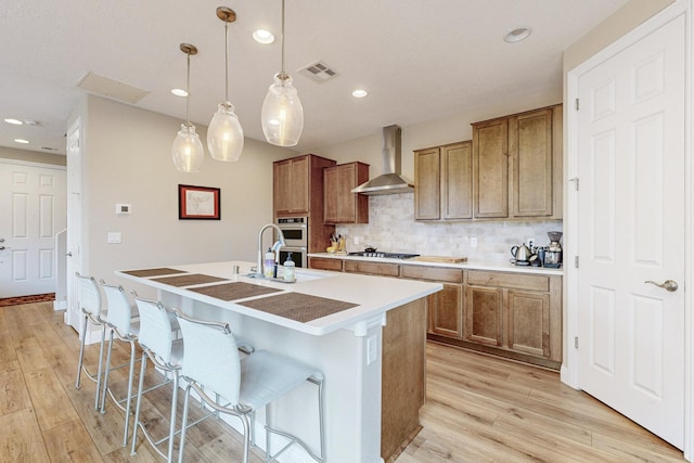 kitchen with wall chimney exhaust hood, tasteful backsplash, an island with sink, decorative light fixtures, and a kitchen bar