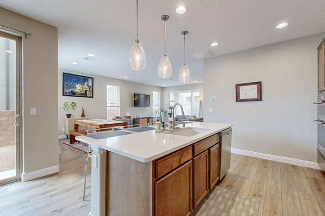 kitchen featuring sink, stainless steel dishwasher, decorative light fixtures, a kitchen island with sink, and light wood-type flooring