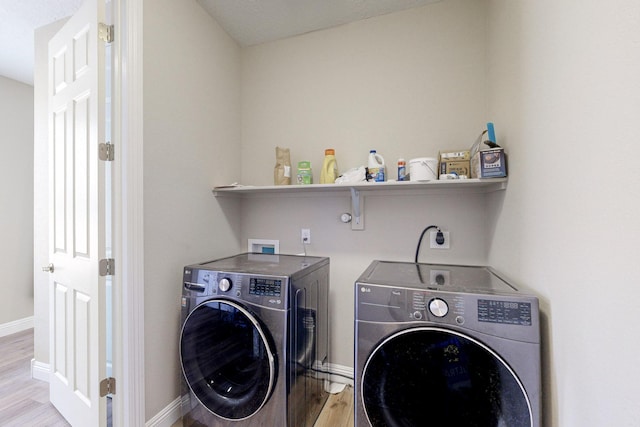 clothes washing area with washing machine and dryer and light hardwood / wood-style flooring