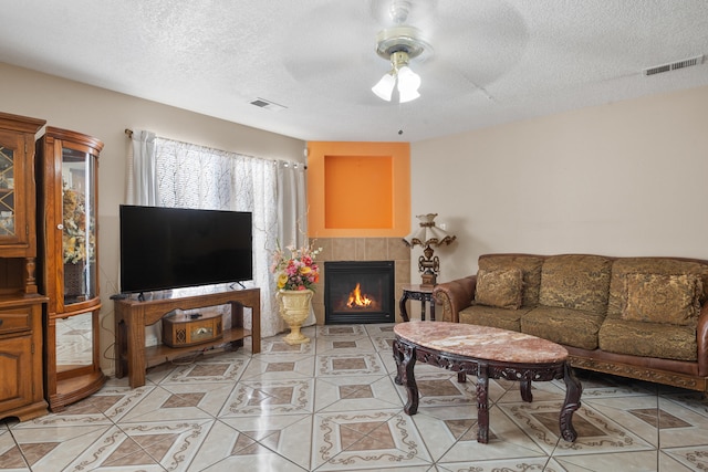 tiled living room with a fireplace, ceiling fan, and a textured ceiling