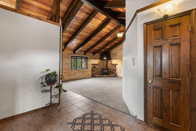 unfurnished living room with wood ceiling, a wood stove, wooden walls, light tile patterned floors, and lofted ceiling with beams