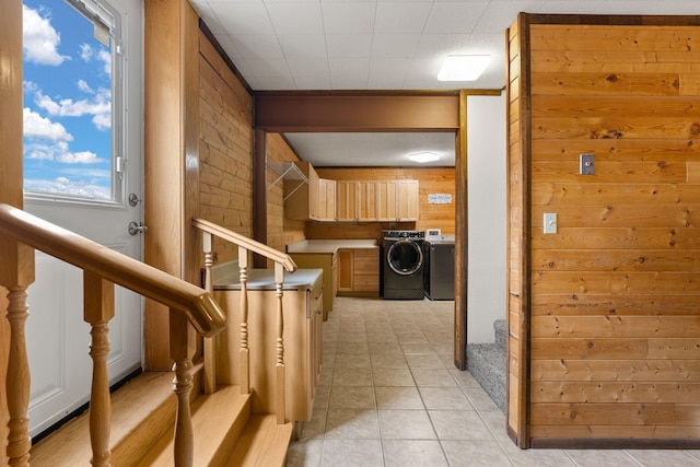 hallway with wooden walls, light tile patterned floors, and separate washer and dryer