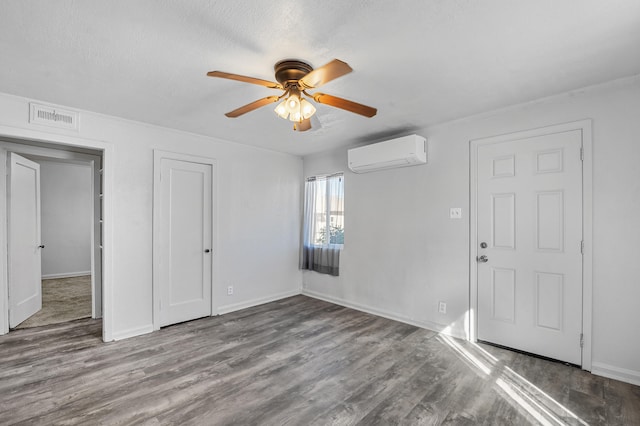 empty room featuring light hardwood / wood-style flooring, a textured ceiling, a wall mounted AC, and ceiling fan